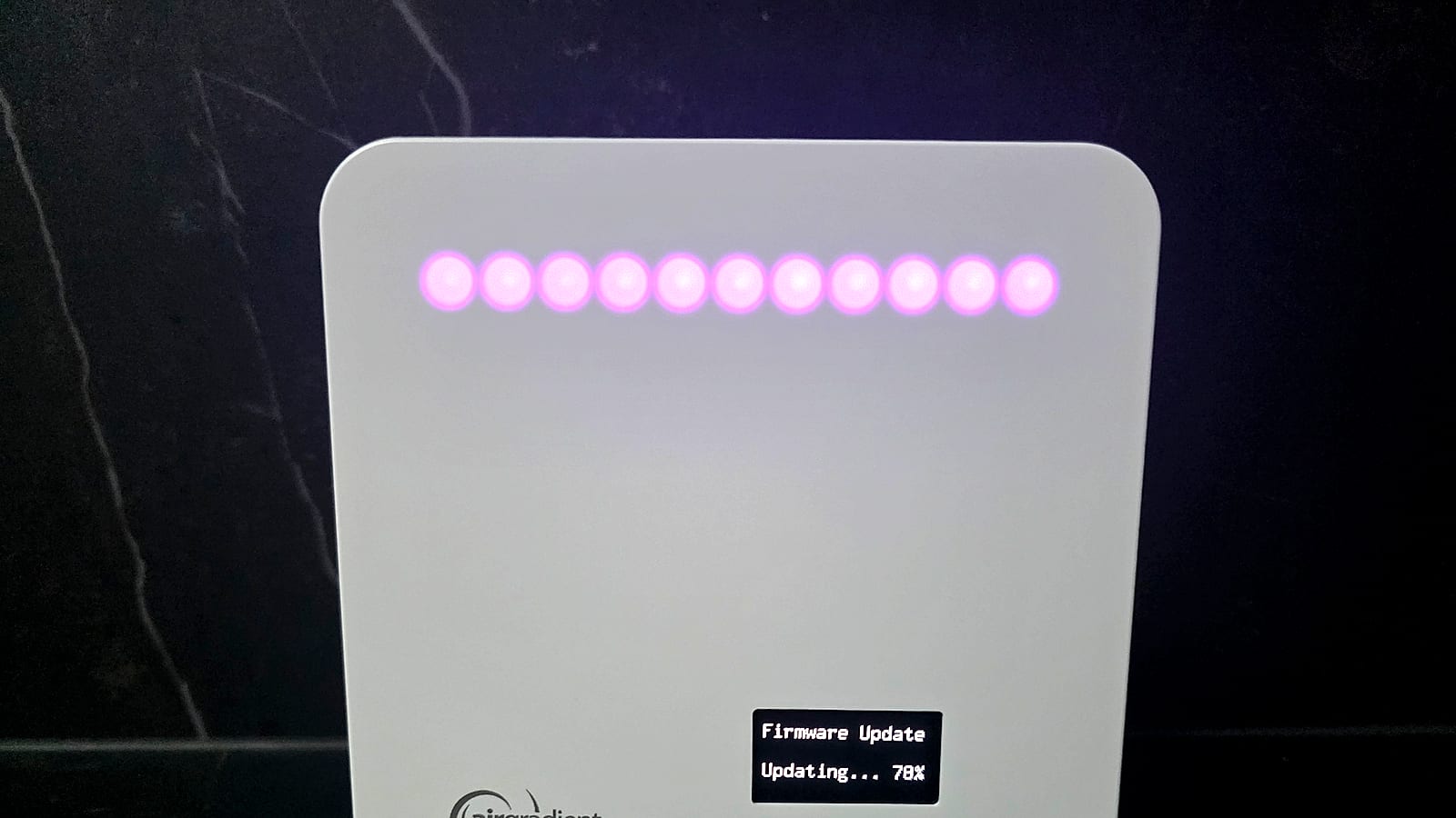 AirGradient ONE with its LED bar lit purple during a firmware update, OLED screen showing update progress